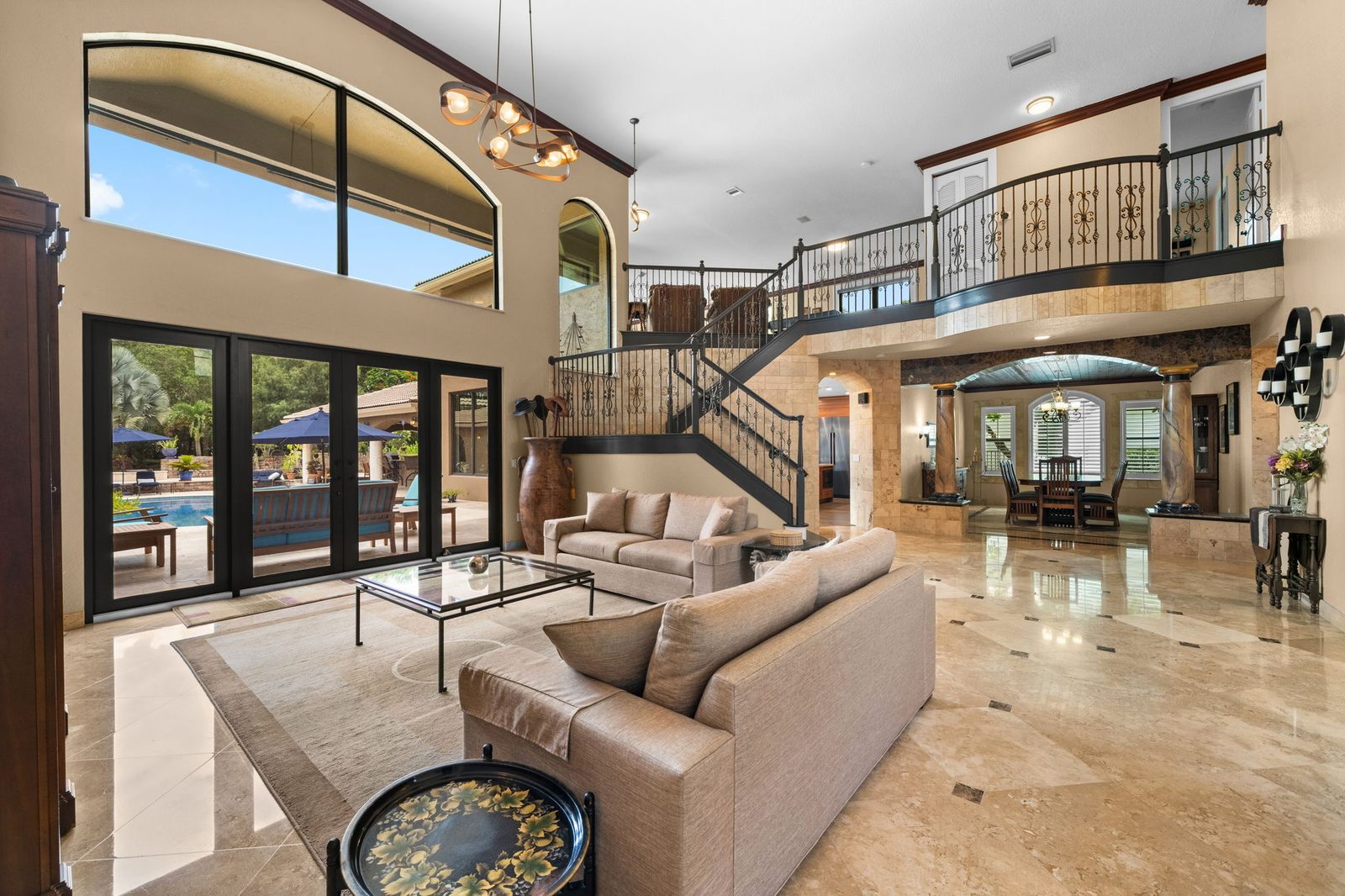 Two-story great room with a sweeping staircase, marble floors and pool views through walls of glass